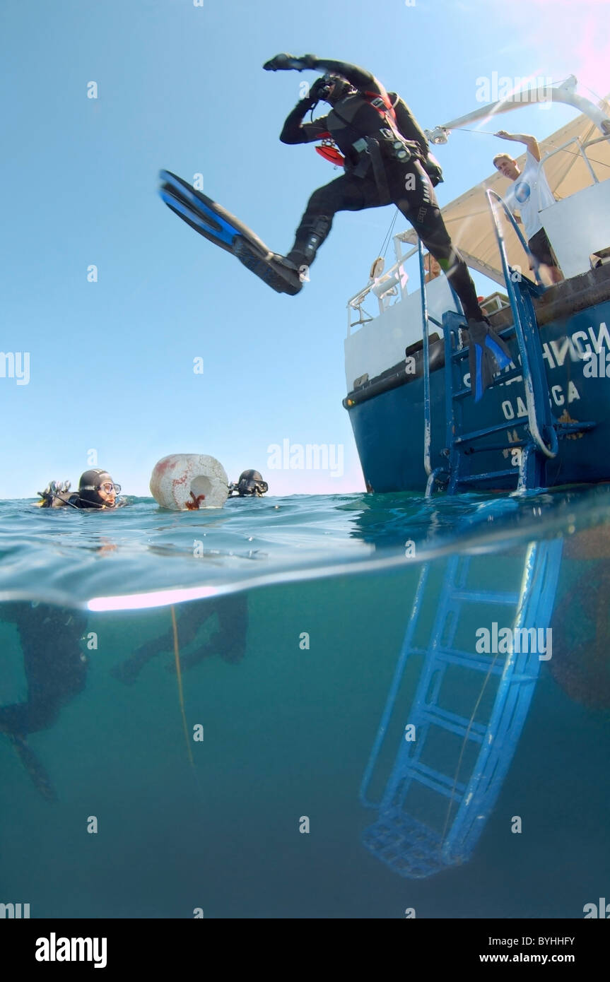 Unterwasser auf 2 Ebenen. Scuba Diver Sprünge im Wasser vom Heck eines Schiffes Stockfoto