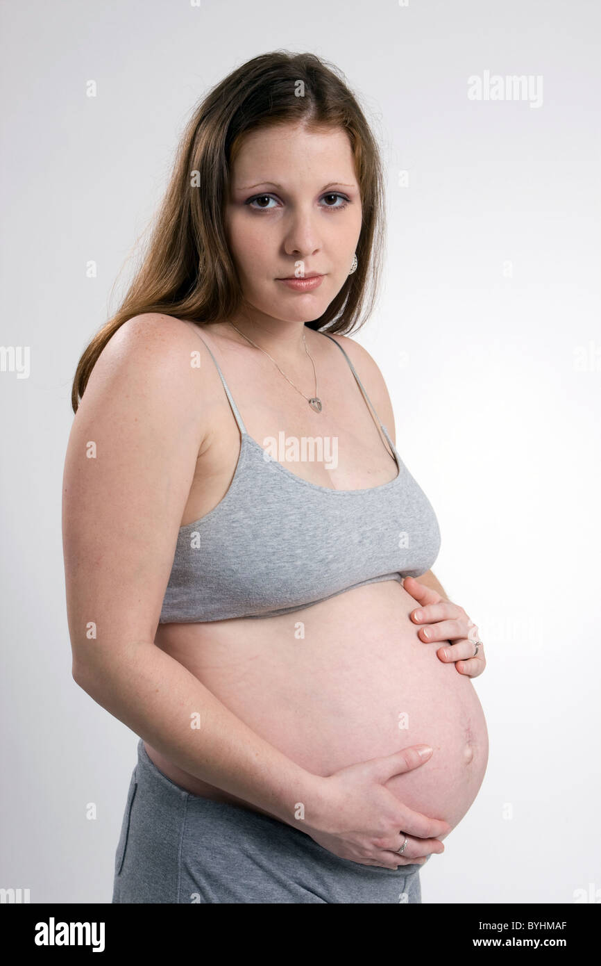 Eine traurige aussehende schwangere Frau, gekleidet in grau hält ihren Bauch. Stockfoto