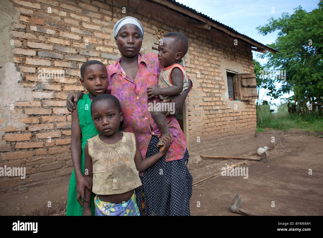 Eine junge alleinerziehende Mutter und ihre Kinder stehen vor ihrer Backstein-Haus in ländlichen Masaka, Uganda, Ostafrika. Stockfoto