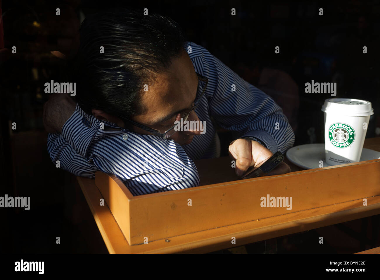 Ein junger Mann Geigen mit seinem geliebten Smartphone nach dem Trinken eines Starbucks-Kaffee im Zentrum von London. Stockfoto