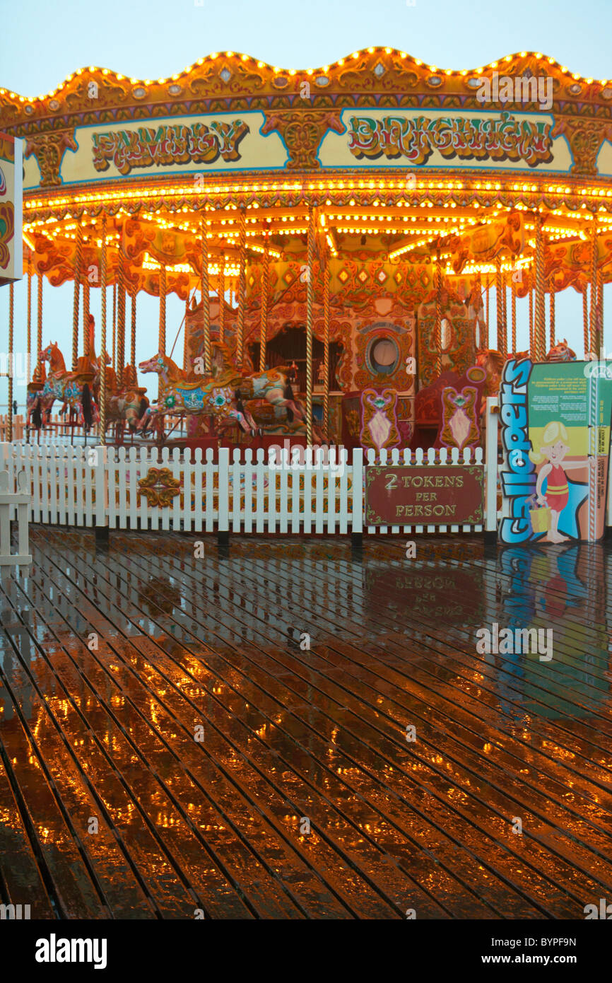 Traditionelle merry Go Runde Fahrgeschäft auf Brightons West Pier. Die Reflexion der Fahrt zeigt in der nassen Promenade. Stockfoto