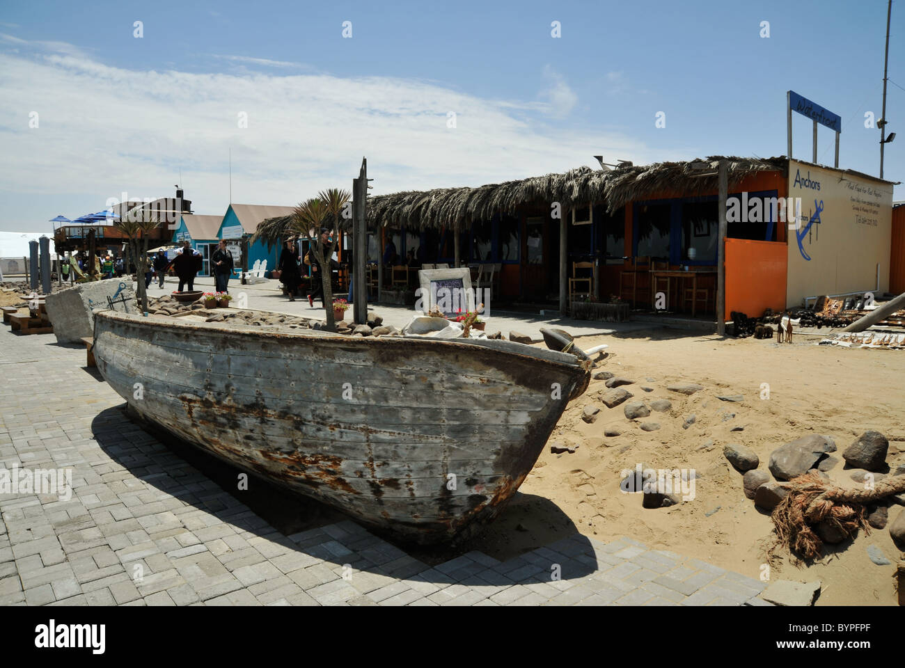 Restaurant und Kuriositätengeschäfte für Touristen, Walvisbay, Erholungshafen, Namibia, altes Holzboot im Vordergrund, Uferpromenade Stockfoto