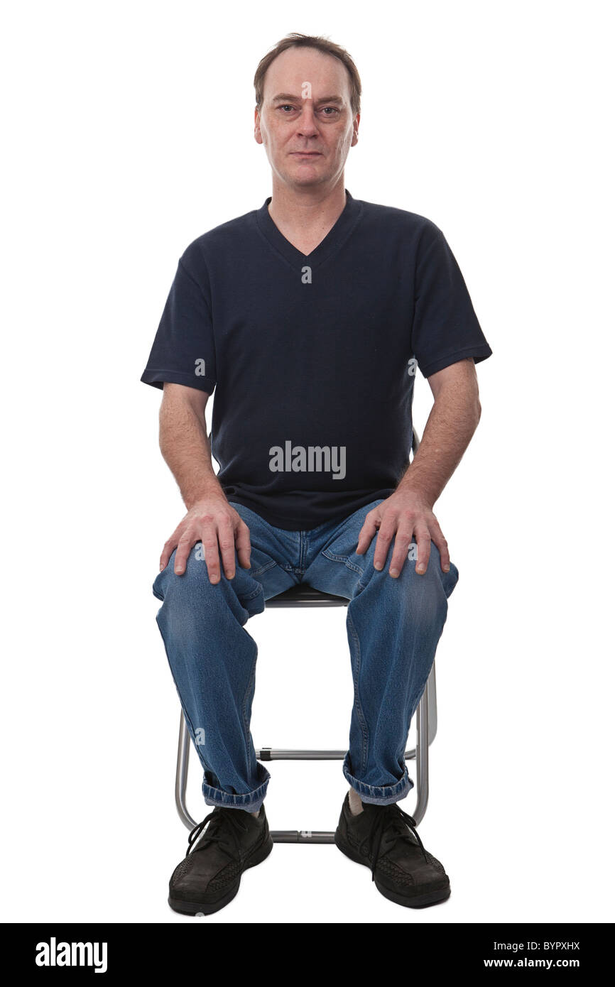 erwachsener Mann gekleidet beiläufig sat auf Stuhl schaut in die Kamera mit Händen auf die Knie, vor einem weißen Hintergrund isoliert Stockfoto