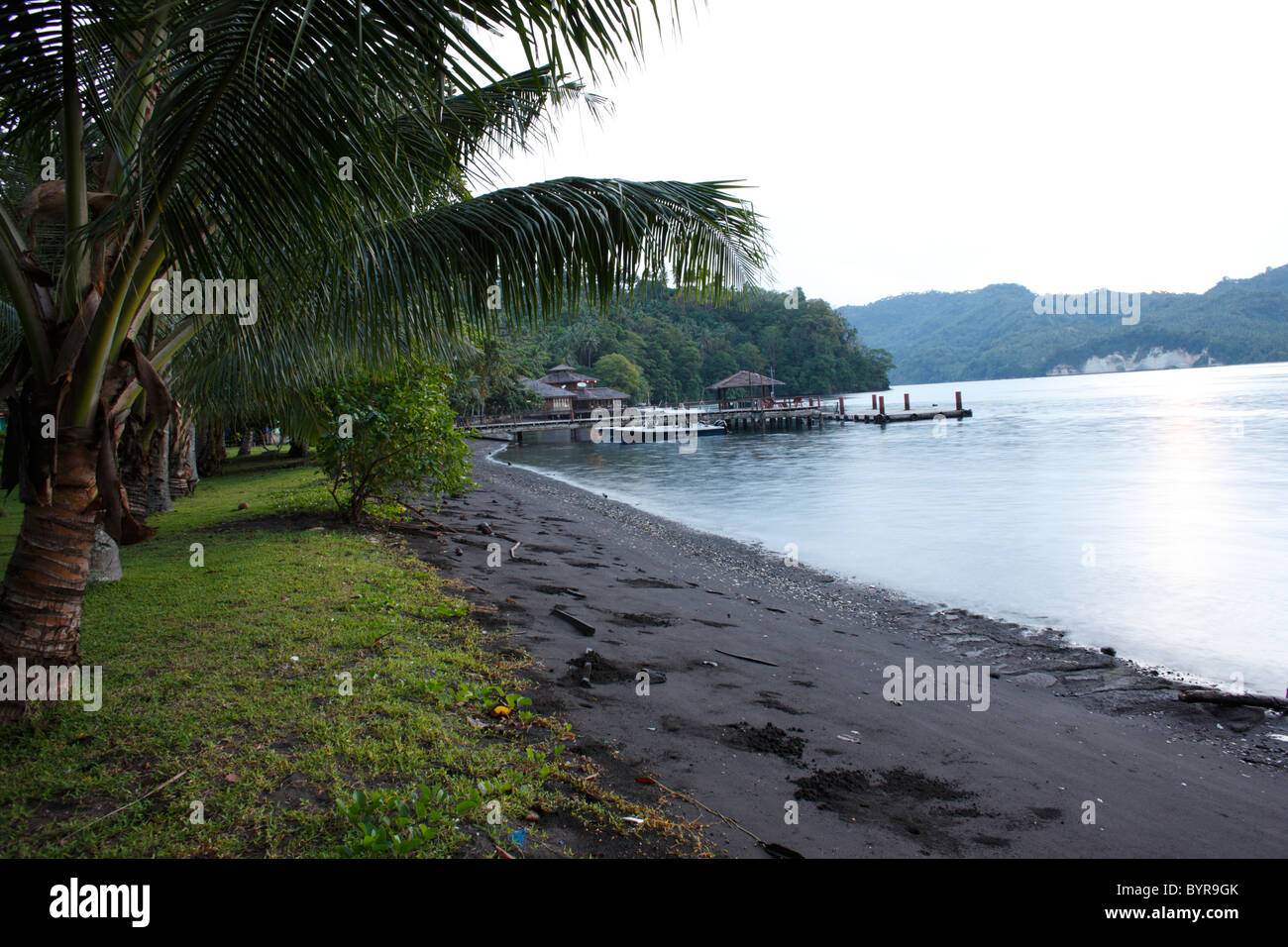 Palmen, Uferlinie der Lembeh Strait und Dock von Kungkungan Bay Resort am frühen Morgen gesehen. Stockfoto