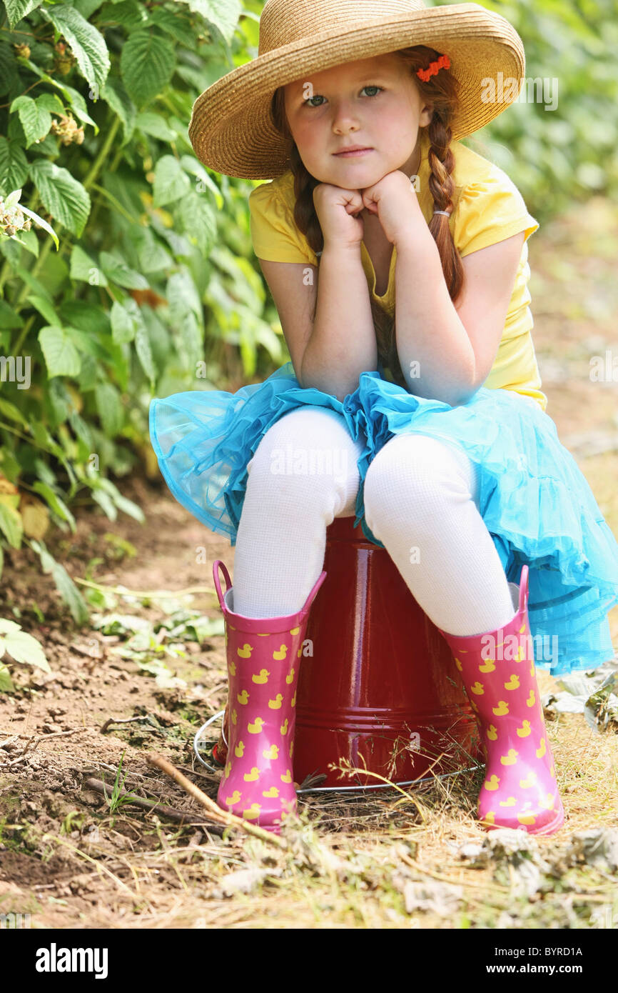 ein Mädchen trägt einen Strohhut und sitzt auf einem großen, roten Eimer; Troutdale, Oregon, Vereinigte Staaten von Amerika Stockfoto