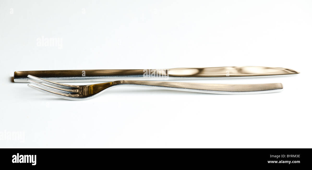 Messer und Gabel aus modernen rostfreien Stahl Design isoliert gegen weiße und reflektierenden golden hellbraun Stockfoto