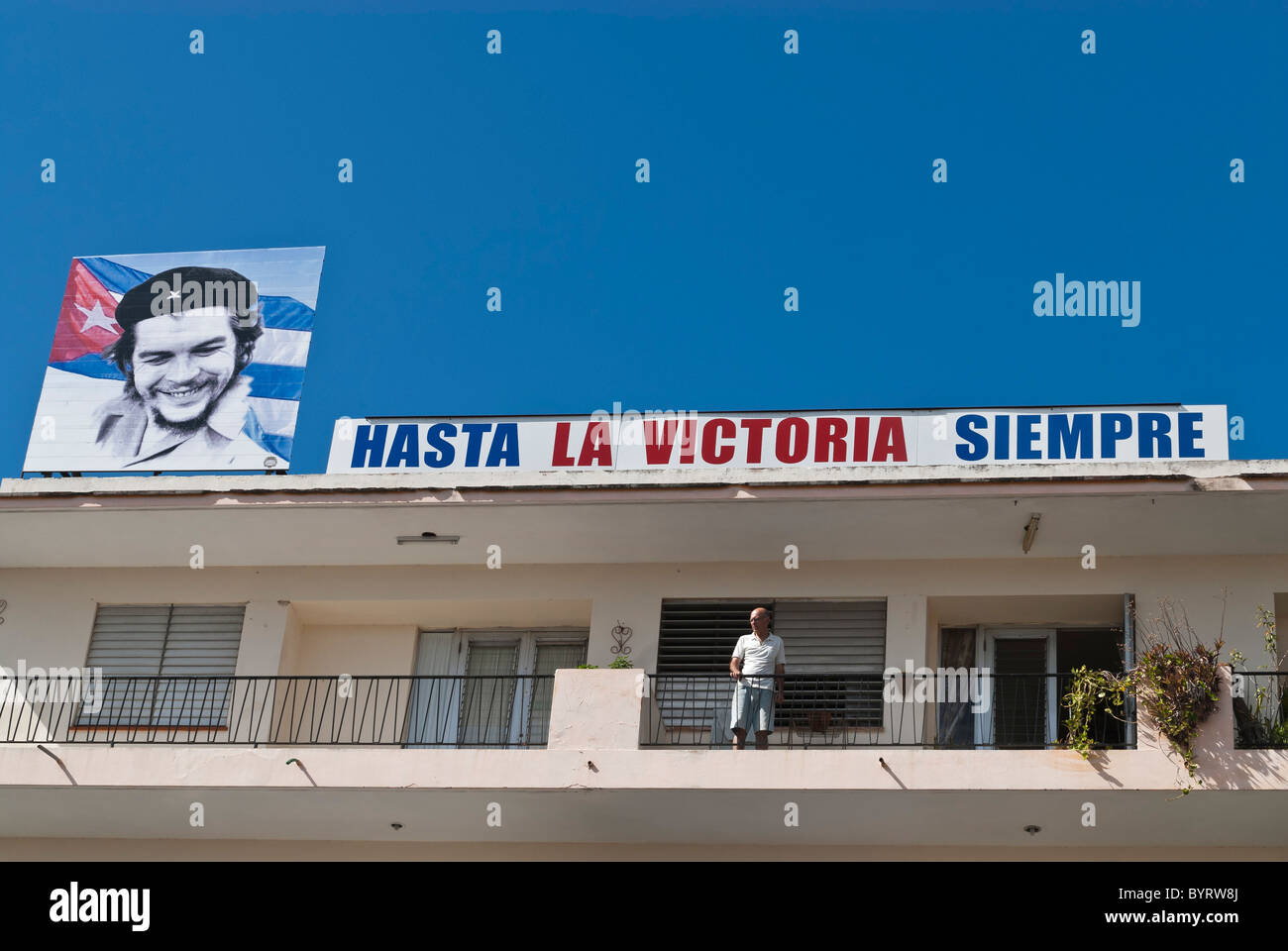 Mann auf einem Balkon und einer kubanischen Propaganda-Zeichen mit dem Bild von Che eine kubanische Flagge. Camagüey, Kuba, Karibik. Stockfoto