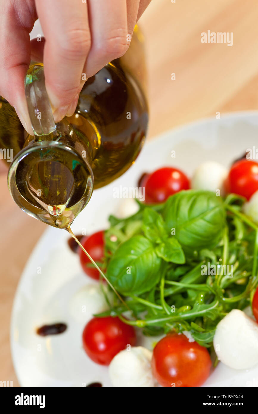 Gießen Öl Salatdressing auf Tomaten, Mozzarella und Rucola-Salat mit Basilikum garnieren und Balsamico-Essig Stockfoto