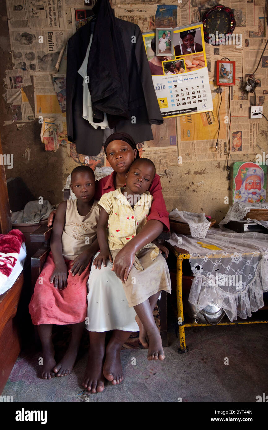 Eine HIV positivere alleinerziehende Mutter sitzt in ihrem Wohnzimmer mit ihren beiden Töchtern in Kampala, Uganda, Ostafrika. Stockfoto