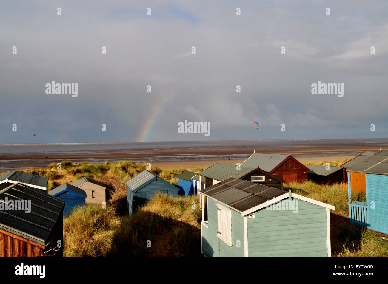 Strandhütten auf der englischen Küste, Regenbogen und Kite-Surfer im Winter Komplementärfarben. Stockfoto