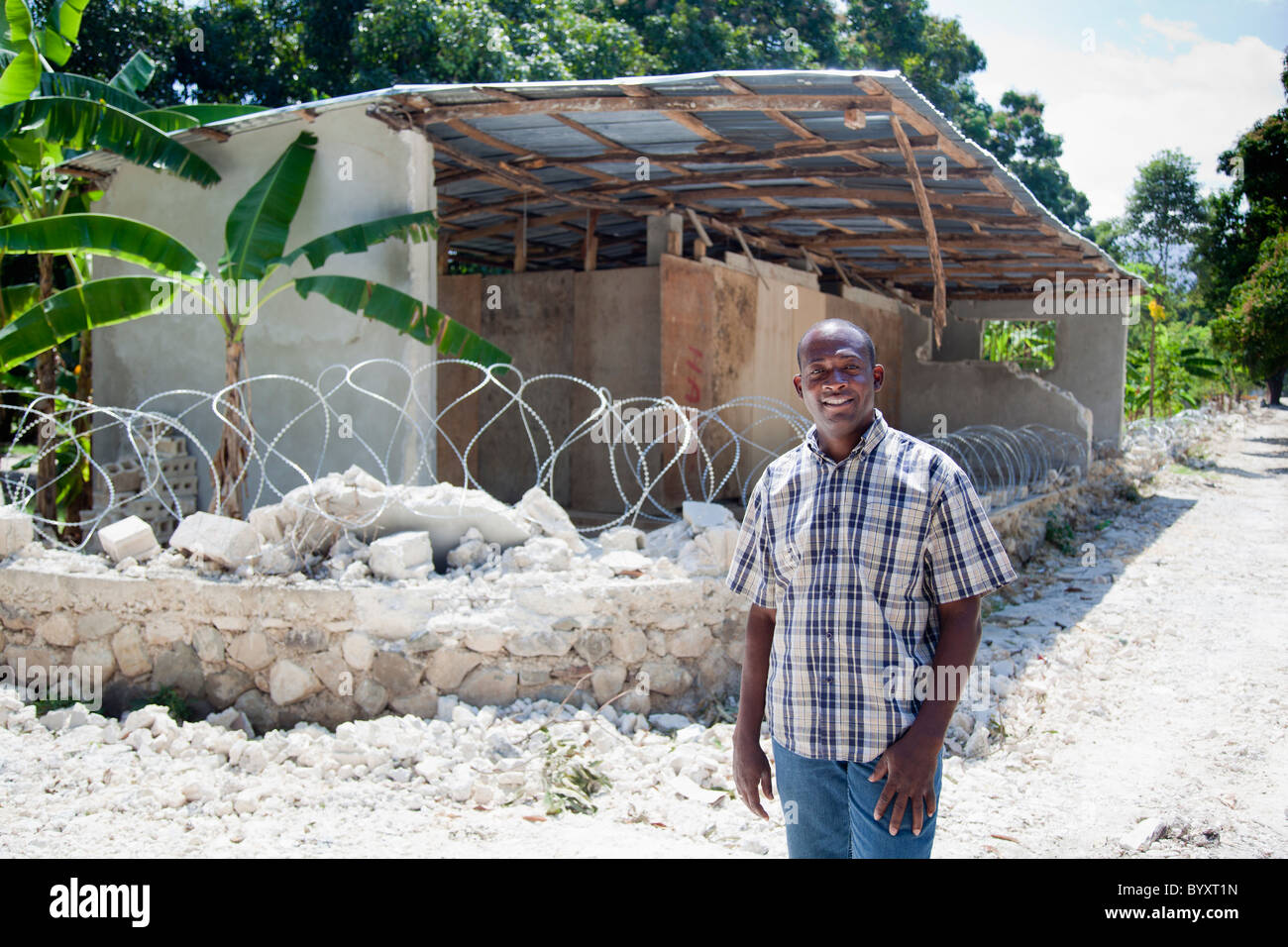 ein Mann steht vor Ruinen und einem Stacheldraht sitting on Top of was eine mehrschalige Wand war; Grand Goave, haiti Stockfoto