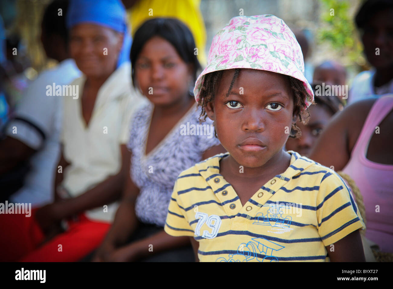 ein Mädchen mit einem traurigen Gesicht und Frauen sitzen hinter ihr in der Hoffnung lebendig Klinik; Grand Saline, haiti Stockfoto