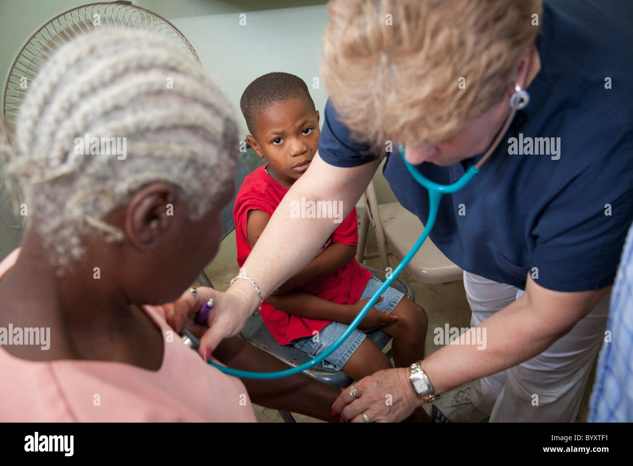 eine Krankenschwester gibt einen Scheck an eine Frau und ein Junge sieht auf; Grand Saline, haiti Stockfoto
