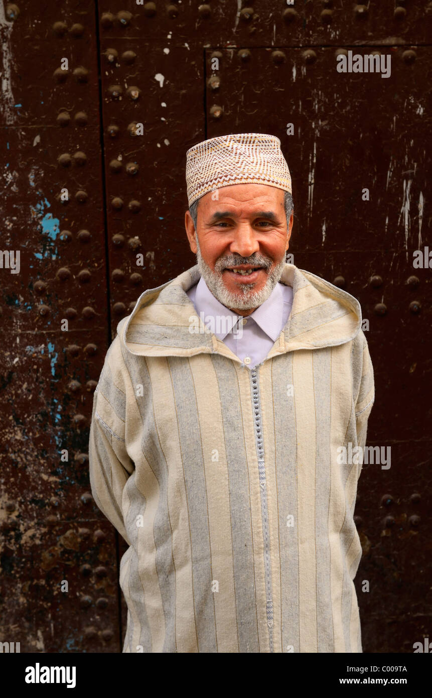Lächelnd marokkanischen Mann in djellaba und Kappe gegen eine alte Tür in Medina von Fes el Bali Marokko Stockfoto
