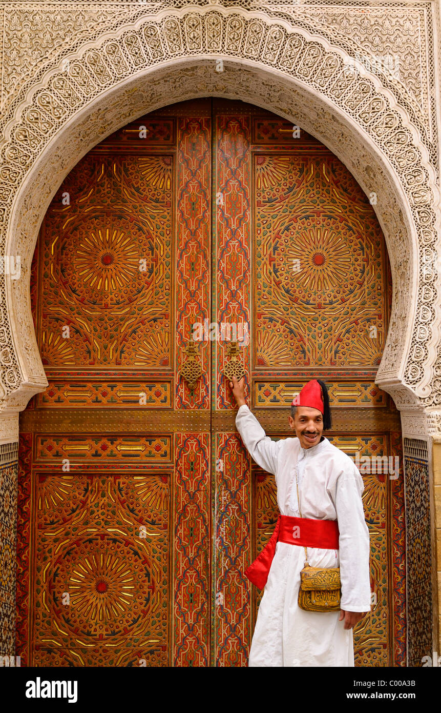 Mann im weißen Gewand und roter Mütze und Schärpe an Tür von Moschee mit komplizierten Steinmetzarbeiten und Farbe in Fes el Bali Medina Fes Marokko Nordafrika Stockfoto