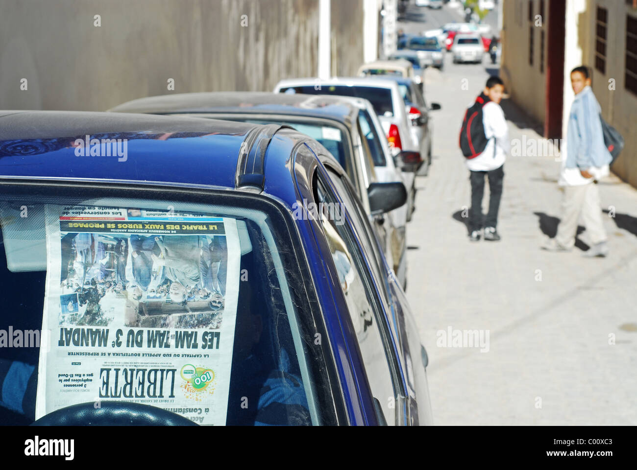 Algerien. Ghardaia, jungen durch parkende Autos in einer Gasse, Zeitung Stucked auf Windschutzscheibe eines Autos im Vordergrund stehen Stockfoto