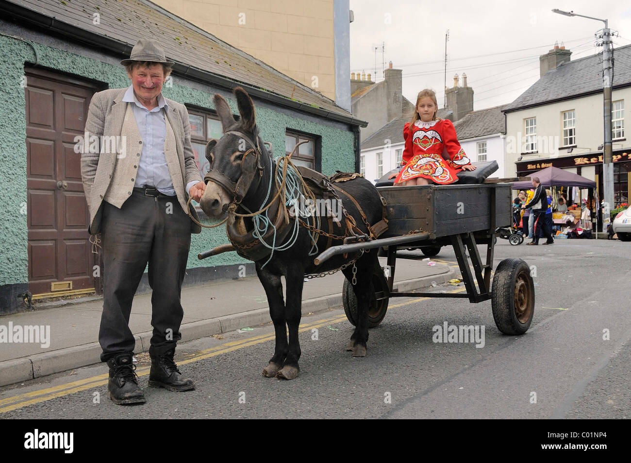 Alter Bauer und Kind tragen moderne keltische Tracht, Mädchen sitzen auf einem traditionellen Eselskarren außerhalb der Partei Sinn Féin Stockfoto