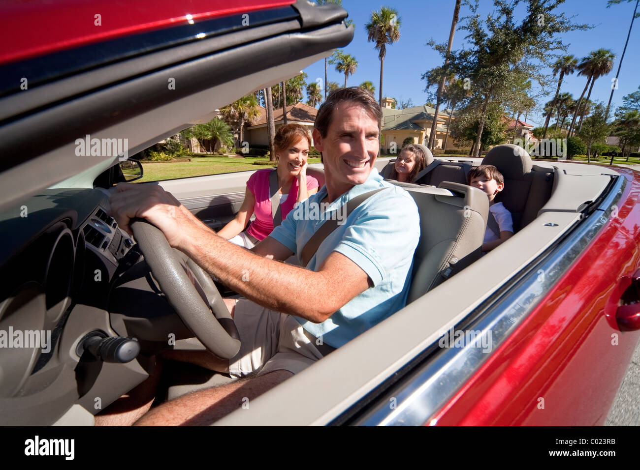 Mann und Frau Eltern und zwei Kinder, die Spaß in einem roten Cabrio bei Sonnenschein fahren Stockfoto