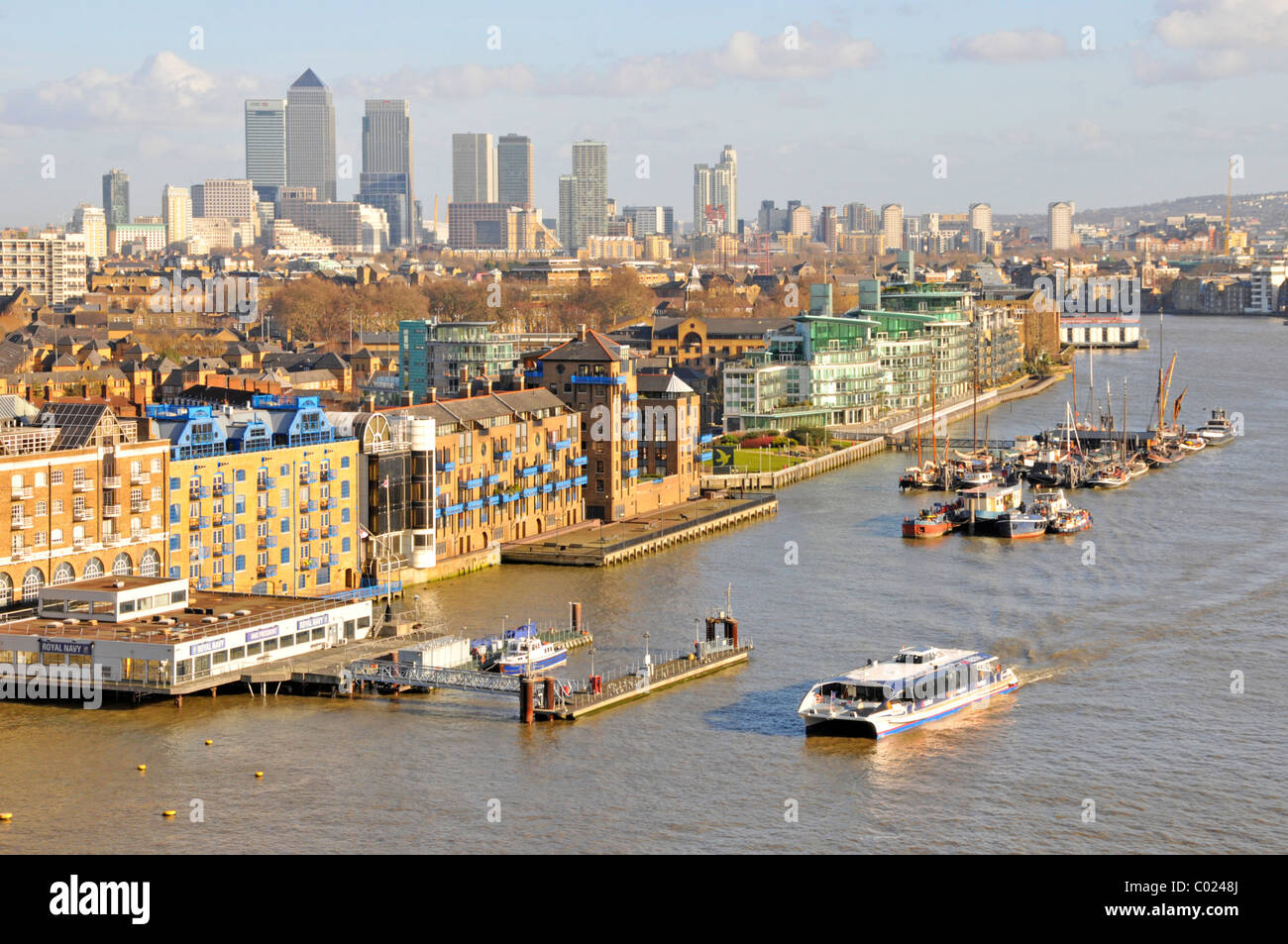 Wasserbus mit Thames Clipper in Tower Hamlets Stadtlandschaft & Pool von London mit Apartmentblöcken am Flussufer und Skyline von Canary Wharf jenseits von England Stockfoto