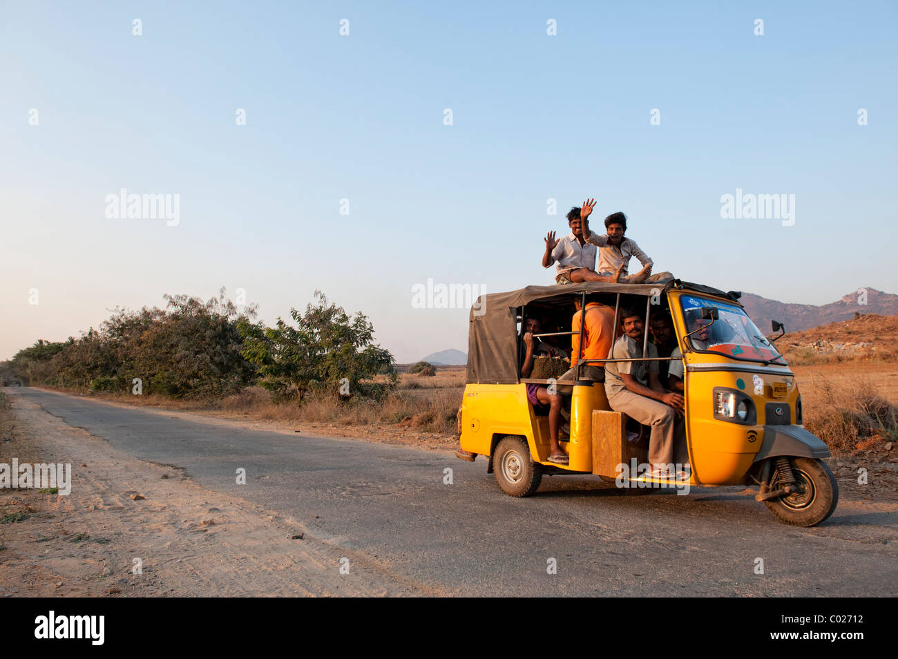 Indische Autorikscha voll von Menschen, mit Passagieren auf dem Dach sitzt entlang einer Landstraße. Andhra Pradesh, Indien Stockfoto