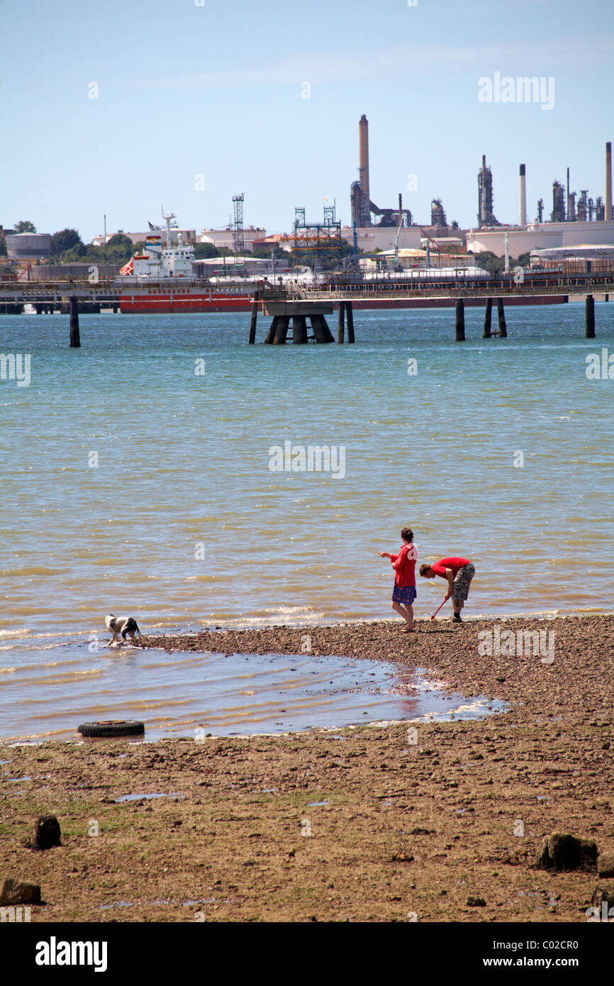 paar Ball spielen mit ihrem Hund am Strand in Hamble mit BP Rohrleitungen und Anlagen in der Ferne im Juli Stockfoto