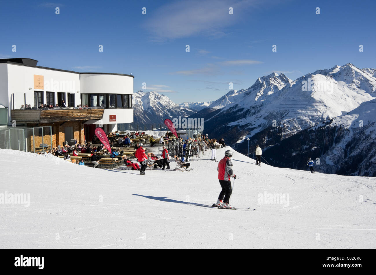 St. Anton am Arleberg, Tirol, Österreich. Skifahrer auf der Piste mit der Galzig Gondel summit Station mit Menschen außerhalb Restaurant Sonnenbad Stockfoto