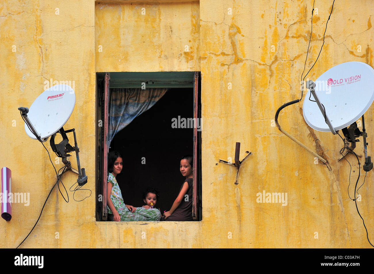 Drei kleine Kinder schauen neugierig aus dem Fenster, Fassade mit Satellitenschüsseln, Meknès, Marokko, Afrika Stockfoto