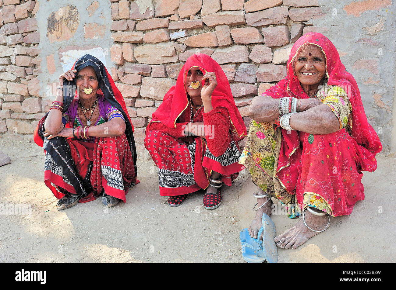 Drei indische Frauen mit goldener Nase-Ringen in traditioneller Kleidung vor einer Steinmauer auf dem Boden sitzen Stockfoto