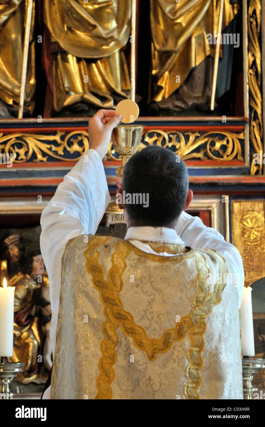 Katholische Priester in der Weihe mit Kelch und Hostie vor einem