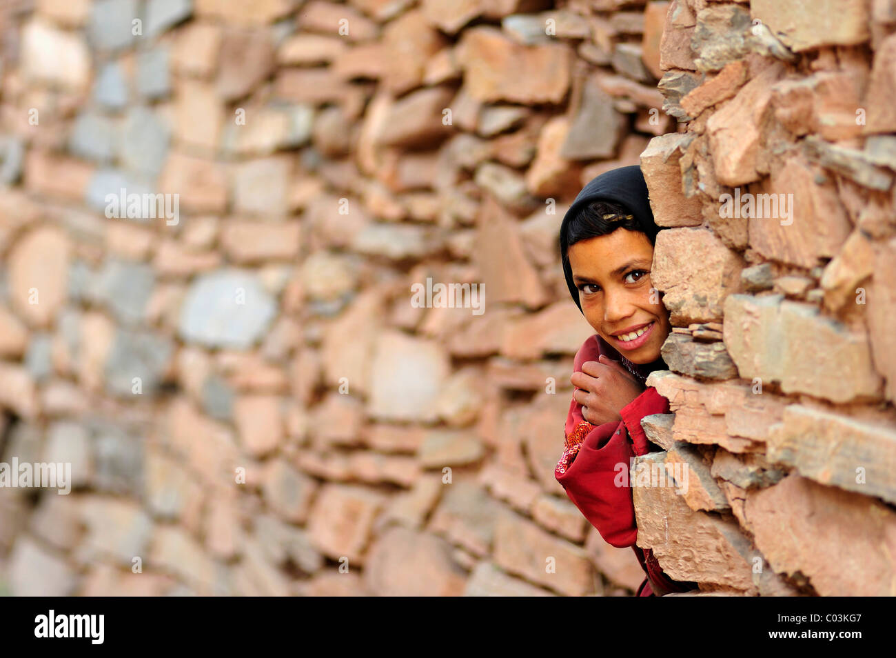 Kleines Mädchen schauen neugierig hinter der Ecke einer Wand Kelaa M'gouna, Atlasgebirge, Marokko, Afrika Stockfoto