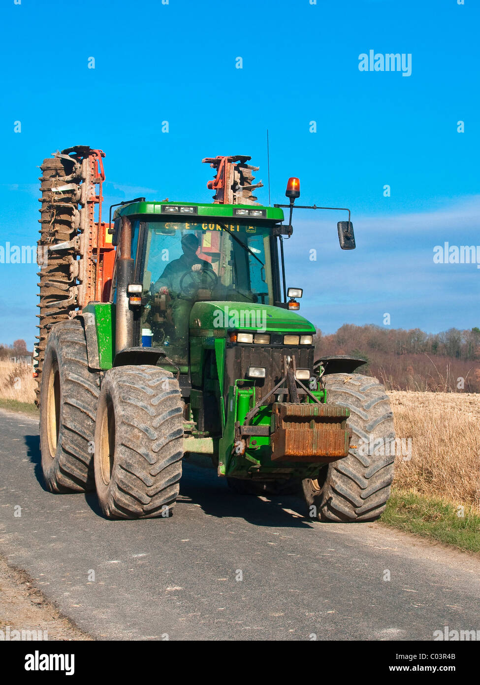 John Deere 8300 Traktor mit Disc-Roller auf Landstraße - Frankreich. Stockfoto