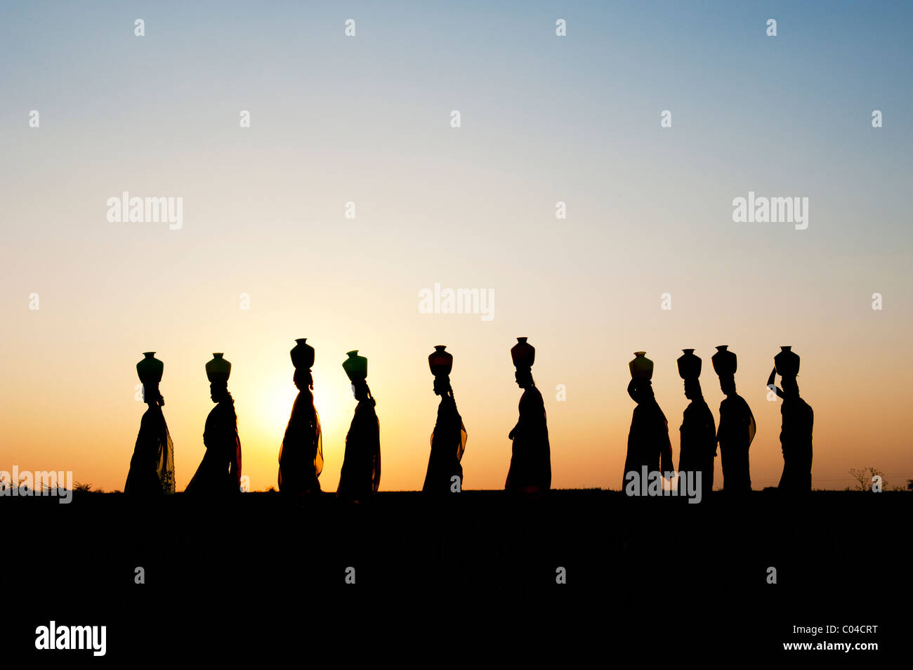 Gruppe von indischen Frauen auf ihren Köpfen in der indischen Landschaft bei Sonnenuntergang mit Wasser Töpfe wandern. Silhouette Stockfoto