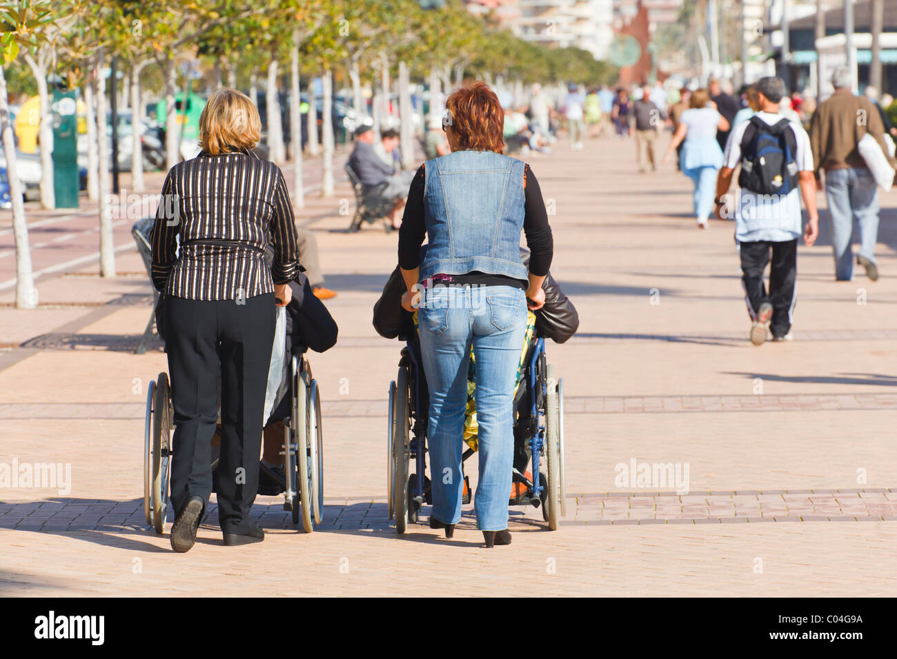 Zwei Frauen schieben Rollstühle auf der Promenade von Los Boliches, Fuengirola, Provinz Malaga, Costa Del Sol, Spanien. Stockfoto