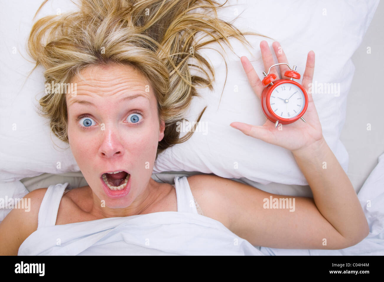 Frau im Bett zu realisieren, dass sie geschlafen hat, trotz des Habens eines Weckers Stockfoto