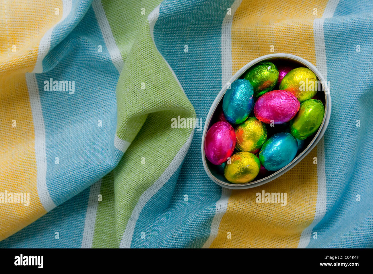 Mini Schokolade Ostereier im Karton Eierkarton auf strukturierte faltige gelbe und Blaue Tischdecke Stockfoto