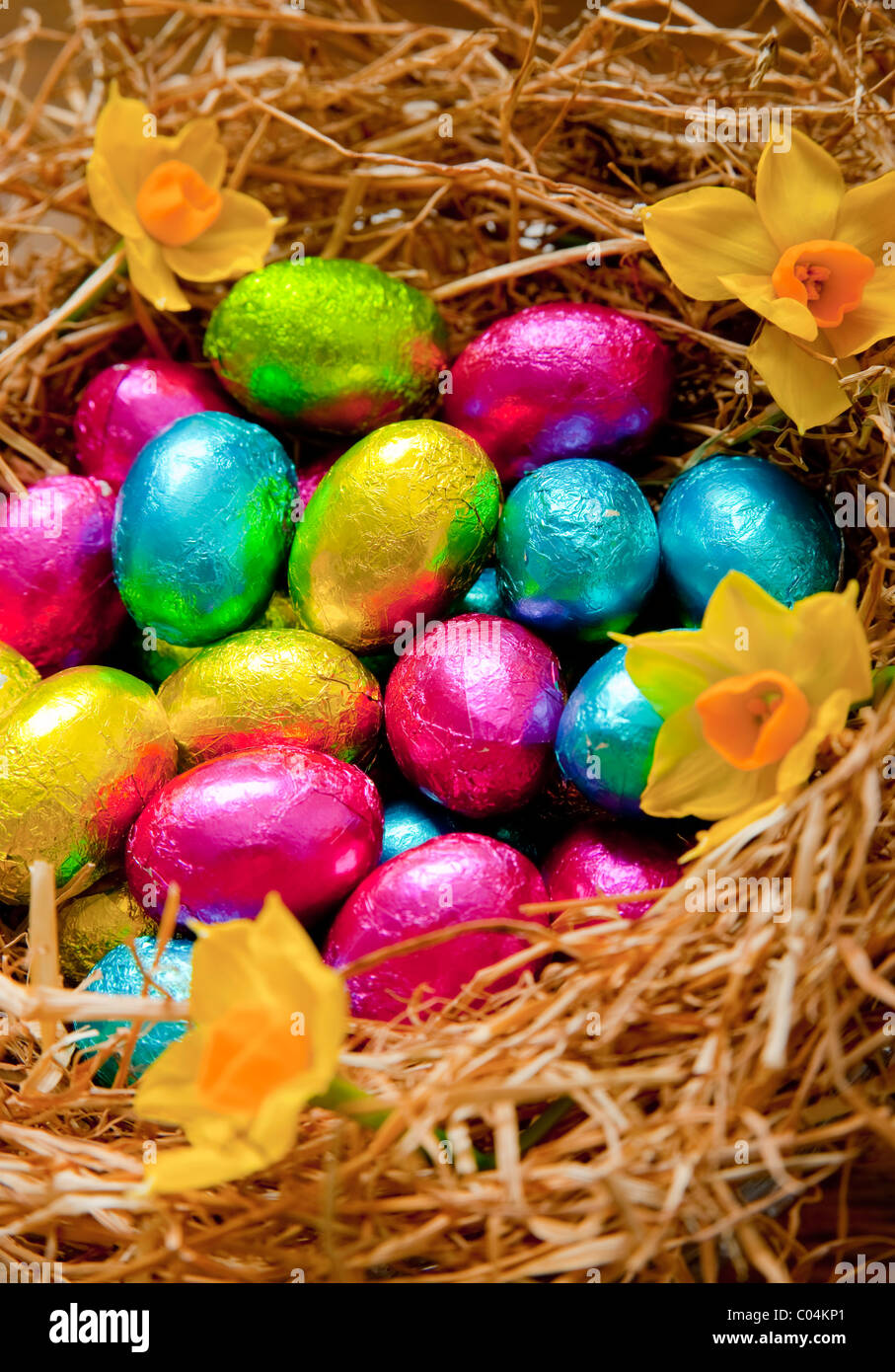 Gruppe von Folie eingewickelt kleine Schokoladeneier in verschiedenen Farben, sitzen in einem Heu, die Vögel auf einen Eichentisch nisten Stockfoto