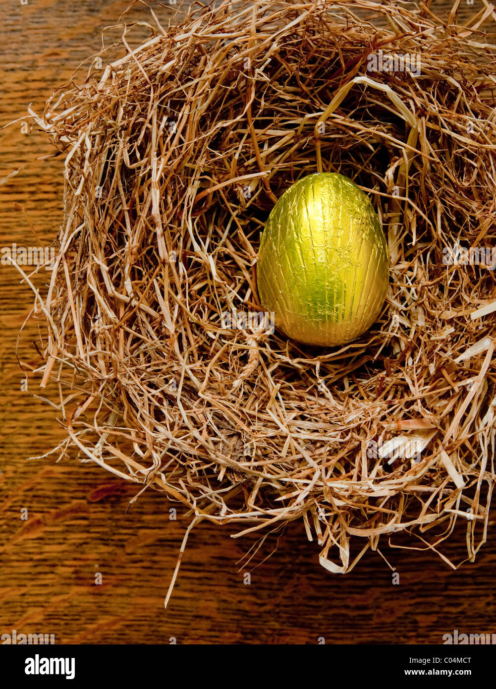 Einzelne Goldfolie gewickelt Schokoladen Osterei in einem Heu, die Vögel auf einen Eichentisch nisten. Stockfoto