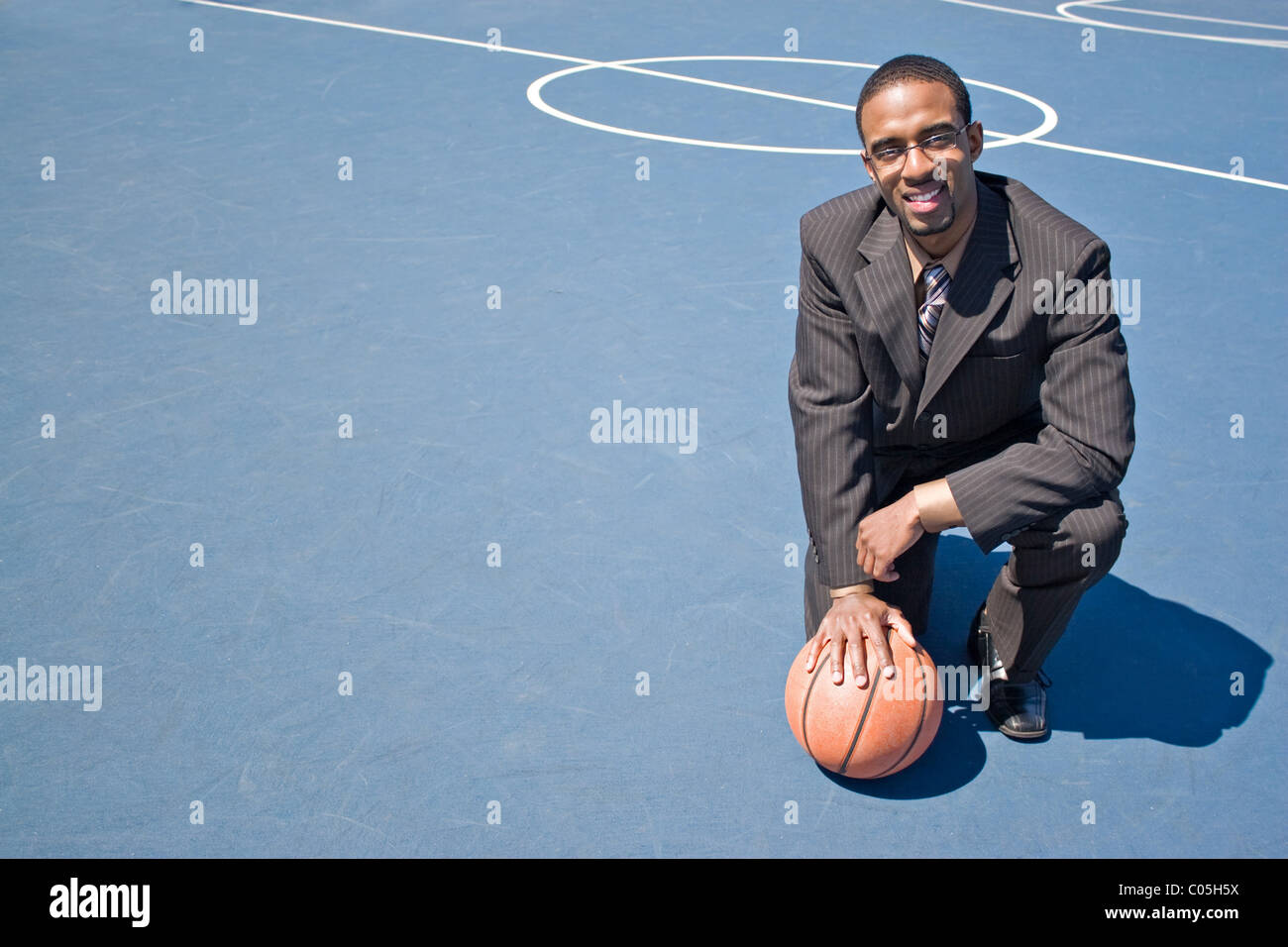 Ein junger Mann im Anzug posiert in dem leeren Basketballplatz mit vielen Exemplar. Stockfoto
