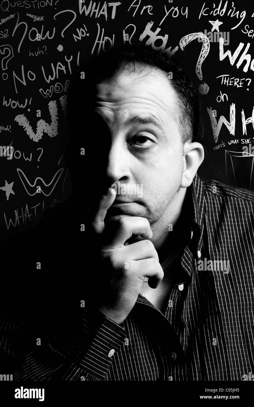 Ein gealterter Mann im Low-Key-Beleuchtung Nachdenken über etwas mit Fragewörtern im Hintergrund - schwarze und weiße Kritzeleien Mitte. Stockfoto