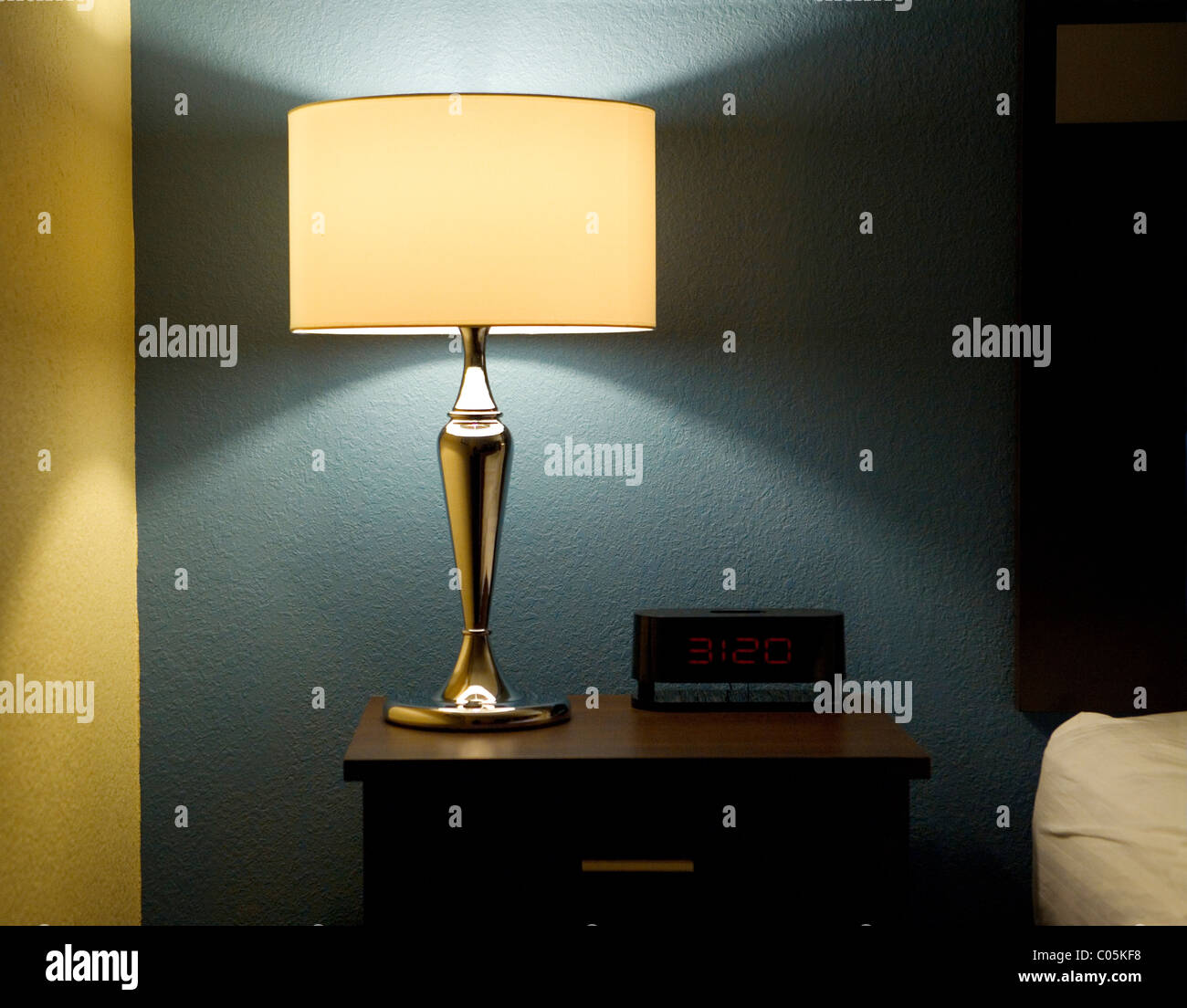 Lampe, Digitaluhr und Beistelltisch neben einem Bett. Stockfoto