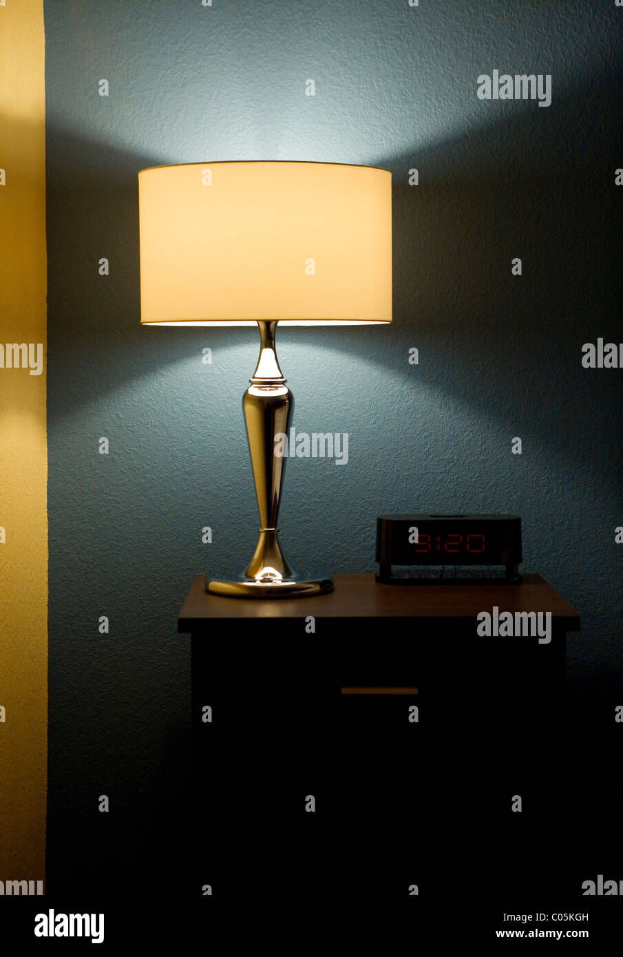 Lampe, Digitaluhr und Beistelltisch neben einem Bett. Stockfoto