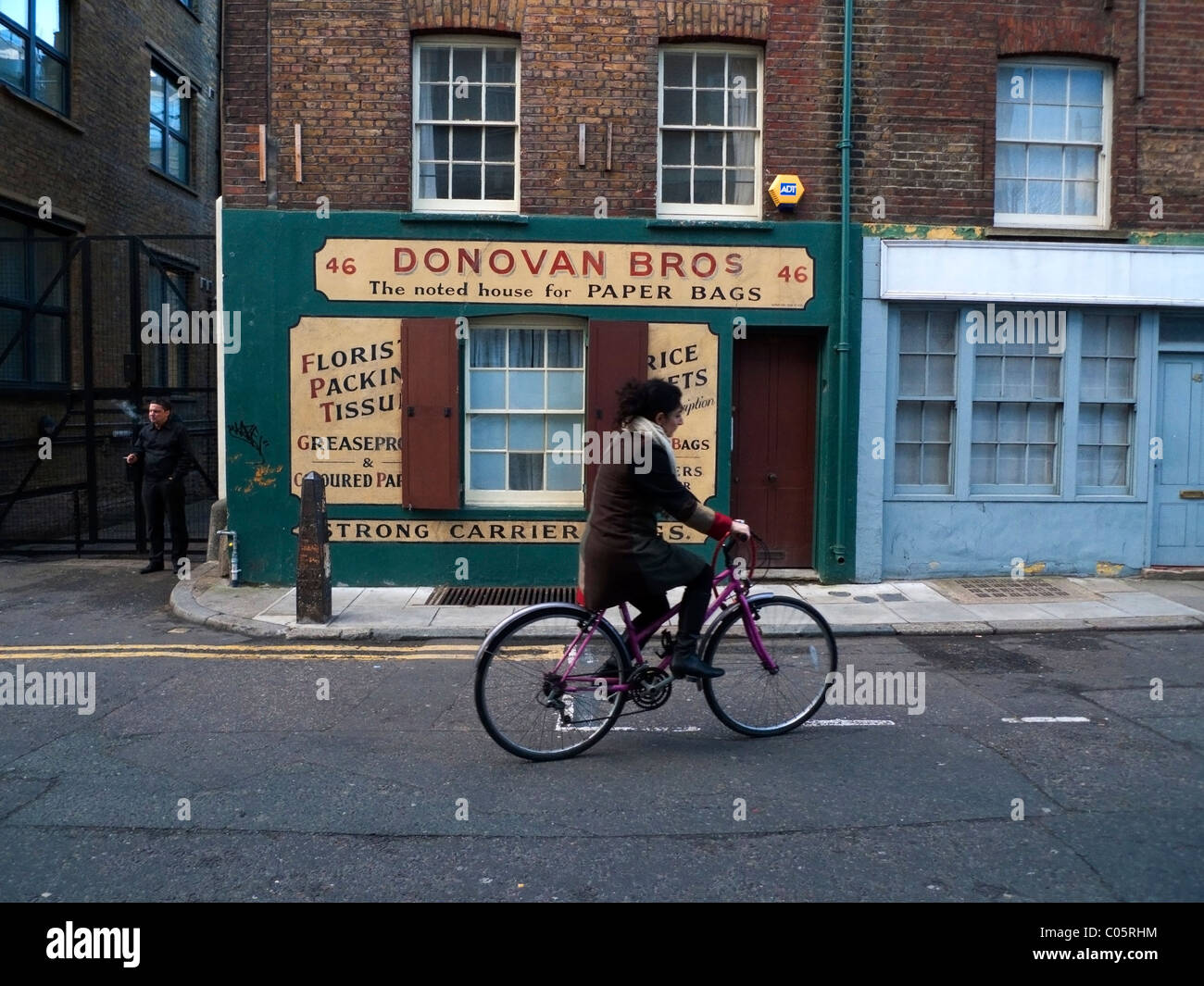 Eine Frau auf einem Fahrrad Radfahren vorbei Donovan Bros Papiertüte Familienunternehmen Shop Spitalfields in East London UK KATHY DEWITT Stockfoto
