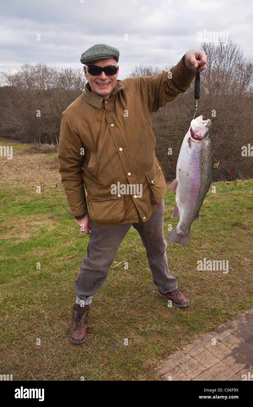 Fischer mit einem großen Regenbogenforellen gefangen in Blackwool Bauernhof Forellen Fischerei, Petworth, Sussex, England, Vereinigtes Königreich. Stockfoto