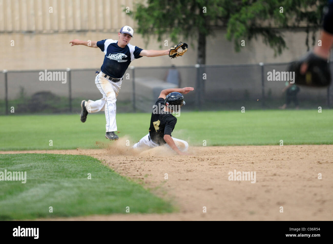Infielder springt über eine verschiebbare Base Runner halten, damit sich die Catcher von im mittleren Feld High School Baseball Spiel USA gehen, werfen. Stockfoto