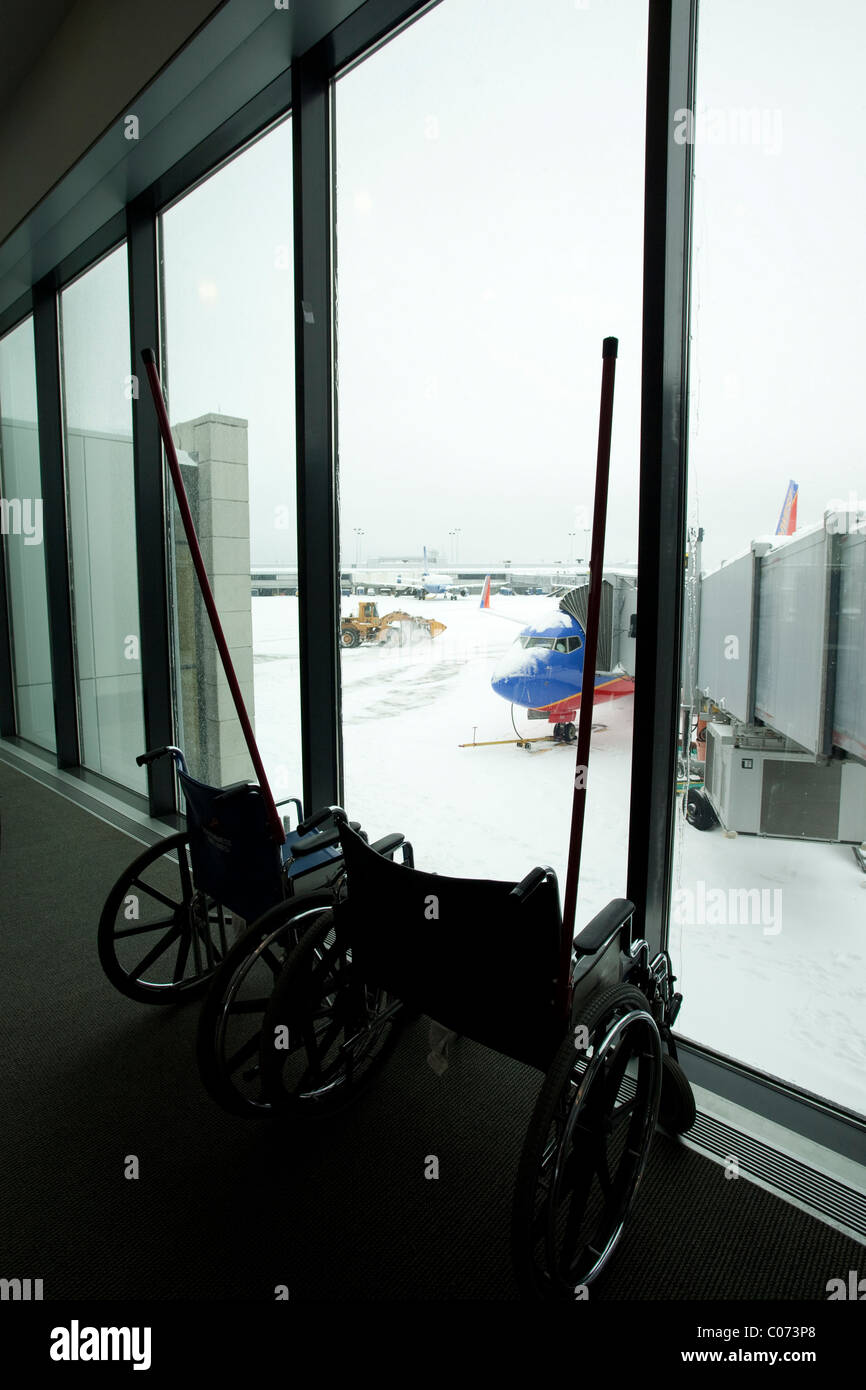 Leeren Rollstuhl sitzen vor einem Fenster mit Blick auf die Räumung von Schnee auf einem geschlossenen Flughafen in Neu-England. Stockfoto