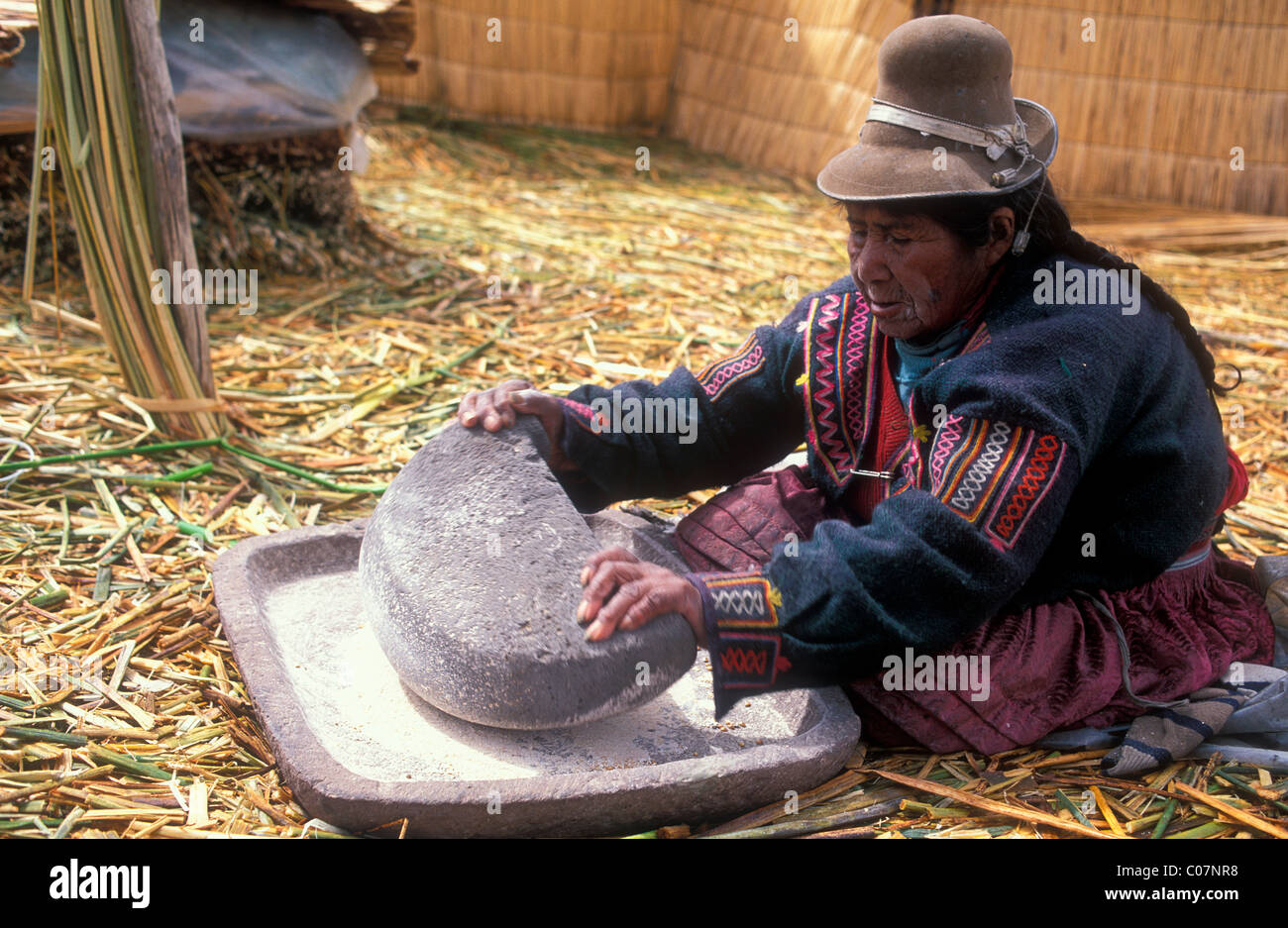 Ältere Frau aus dem Aymara indigenen Volk zermahlen Mais in Flou mit einem Schleifstein, Schilf-Insel aus Totora-Schilf hergestellt Stockfoto