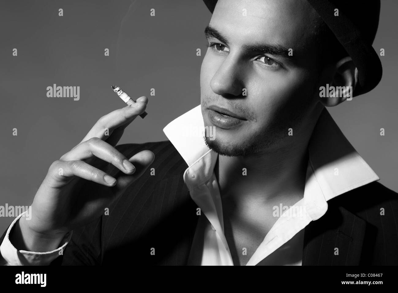 Junger Mann in Anzug, Hemd, Krawatte und Hut eine Zigarette in der Hand halten Stockfoto