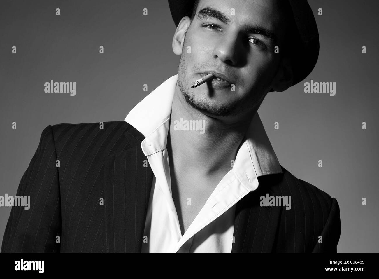 Junger Mann in Anzug, Hemd, Krawatte und Hut, mit einer Zigarette im Mund und einen coolen look Stockfoto