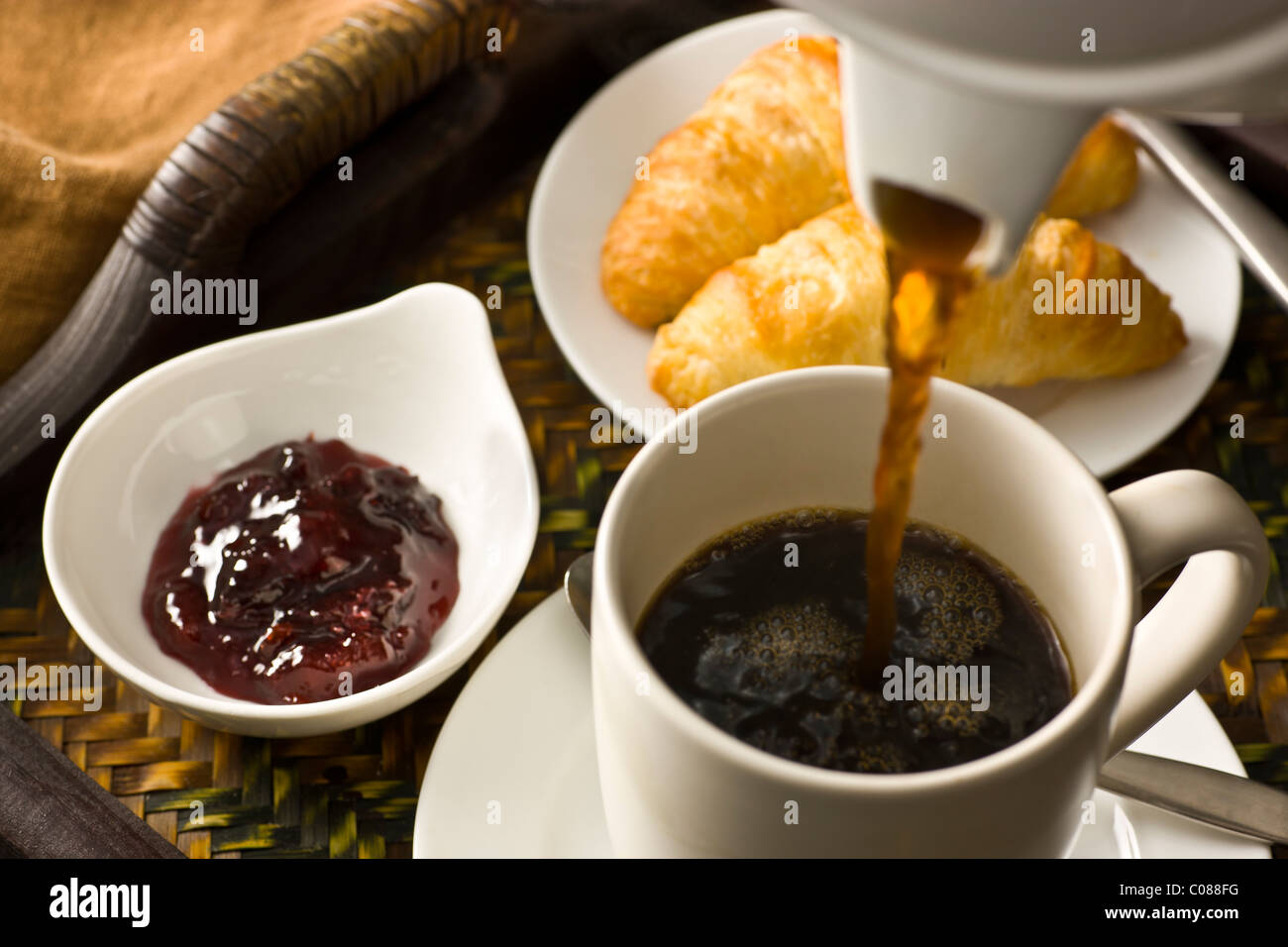 Ein Tablett mit Croissants, Marmelade und eine Tasse heißen schwarzen Kaffee gegossen Stockfoto