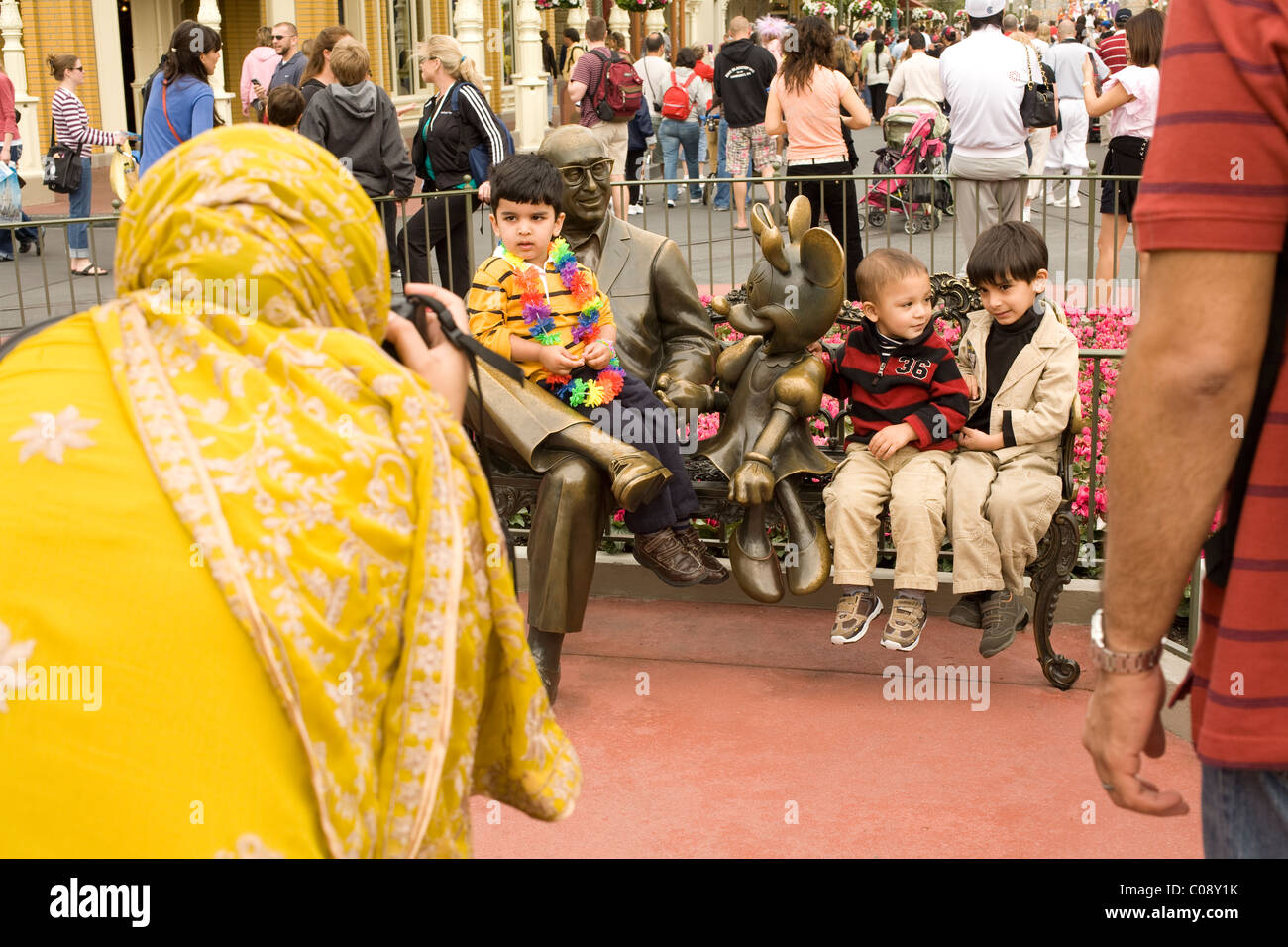 Muslimische Mutter nimmt Fotos ihrer Familie sitzen mit Bronze-Statue von Walt Disney in Disney World in Orlando, Florida. Stockfoto